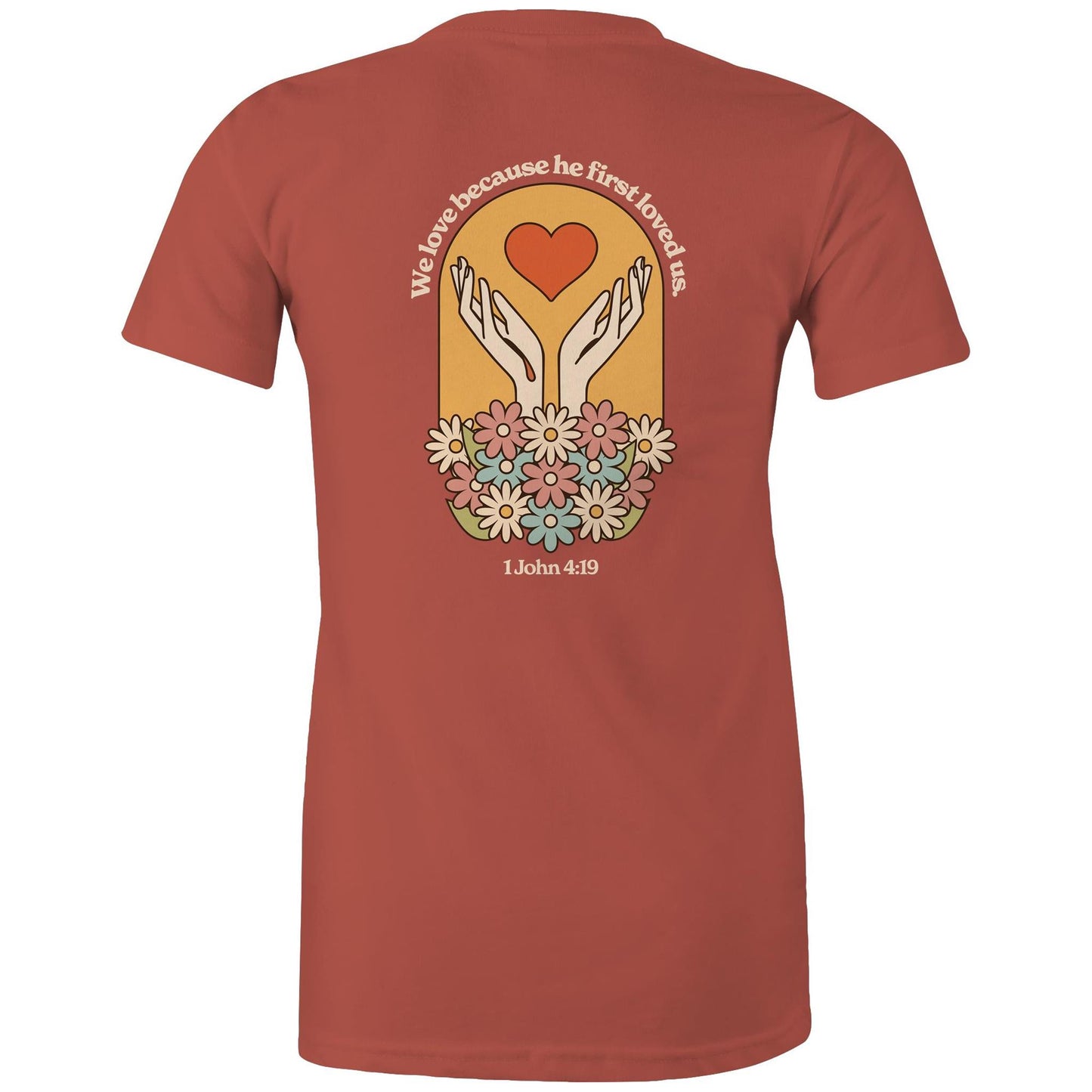 Christian t-shirt with bold faith-based design on the back featuring a red heart, outstretched hands, and colorful flowers. Includes the Bible verse “We love because he first loved us – 1 John 4:19.” Designed by Lighthouse Christian Clothing to inspire love and faith.