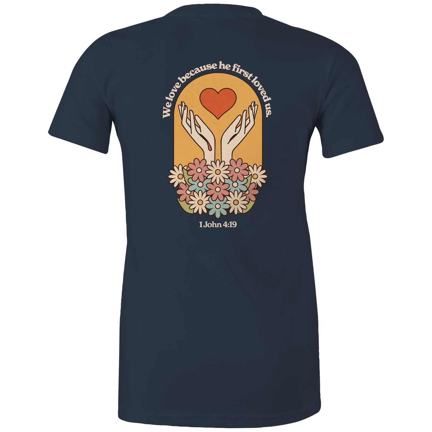 Christian t-shirt with bold faith-based design on the back featuring a red heart, outstretched hands, and colorful flowers. Includes the Bible verse “We love because he first loved us – 1 John 4:19.” Designed by Lighthouse Christian Clothing to inspire love and faith.
