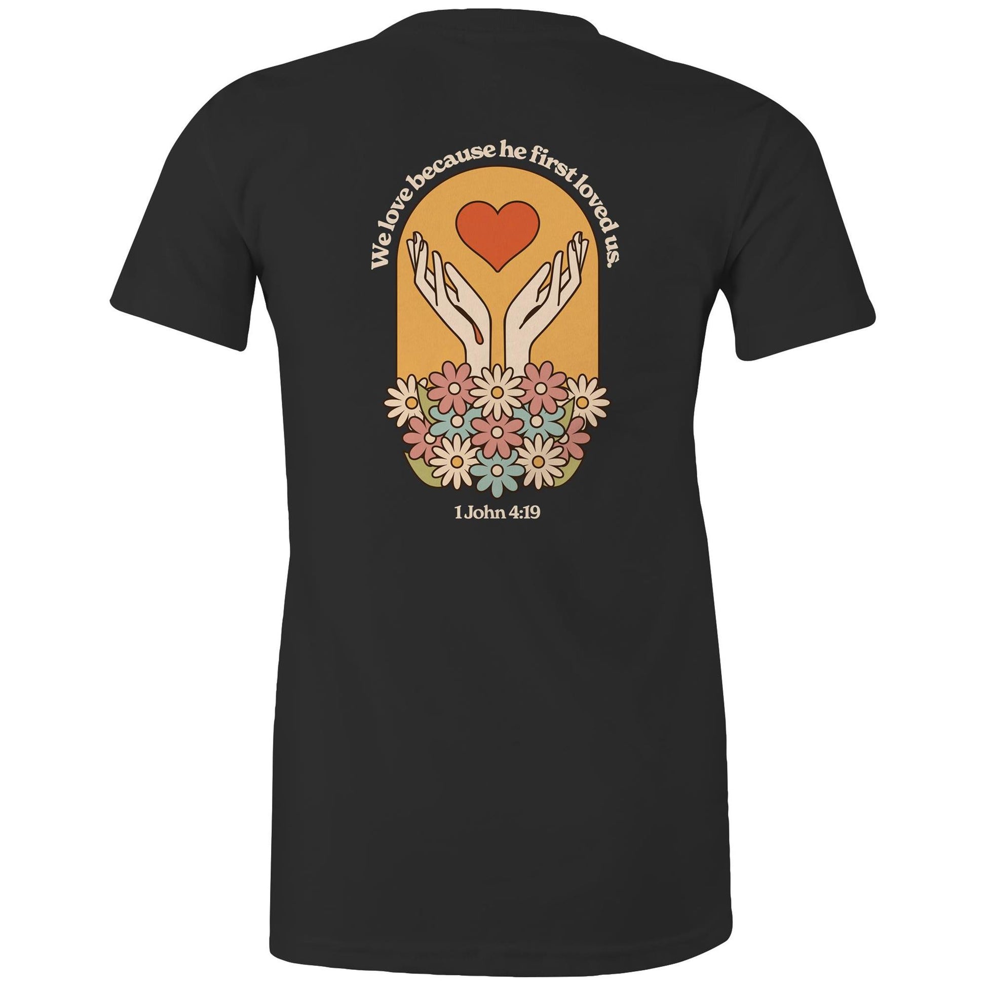 Christian t-shirt with bold faith-based design on the back featuring a red heart, outstretched hands, and colorful flowers. Includes the Bible verse “We love because he first loved us – 1 John 4:19.” Designed by Lighthouse Christian Clothing to inspire love and faith.