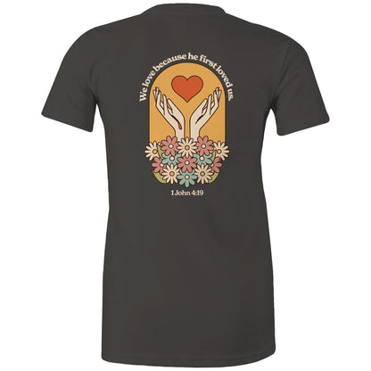 Christian t-shirt with bold faith-based design on the back featuring a red heart, outstretched hands, and colorful flowers. Includes the Bible verse “We love because he first loved us – 1 John 4:19.” Designed by Lighthouse Christian Clothing to inspire love and faith.