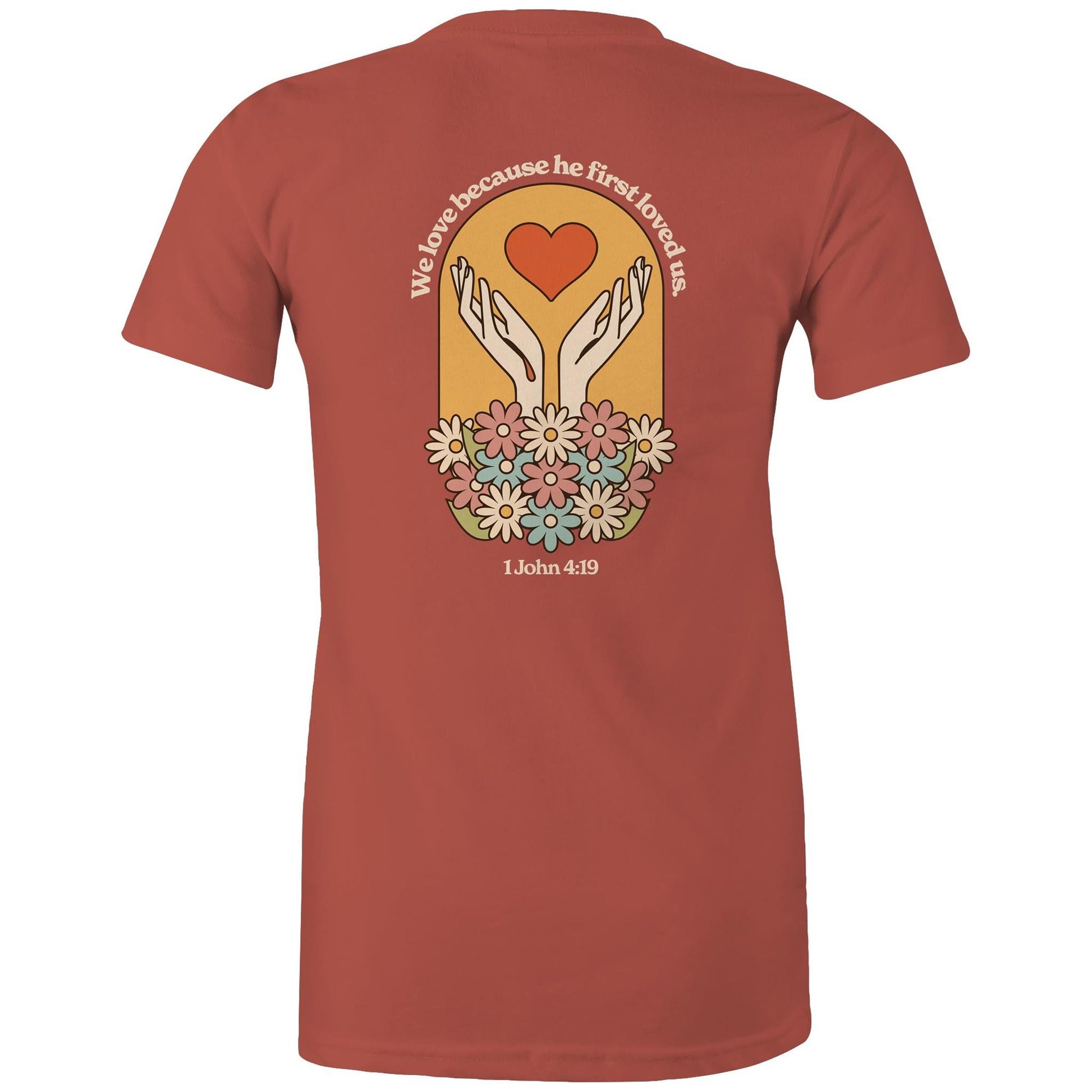 Christian t-shirt with bold faith-based design on the back featuring a red heart, outstretched hands, and colorful flowers. Includes the Bible verse “We love because he first loved us – 1 John 4:19.” Designed by Lighthouse Christian Clothing to inspire love and faith.