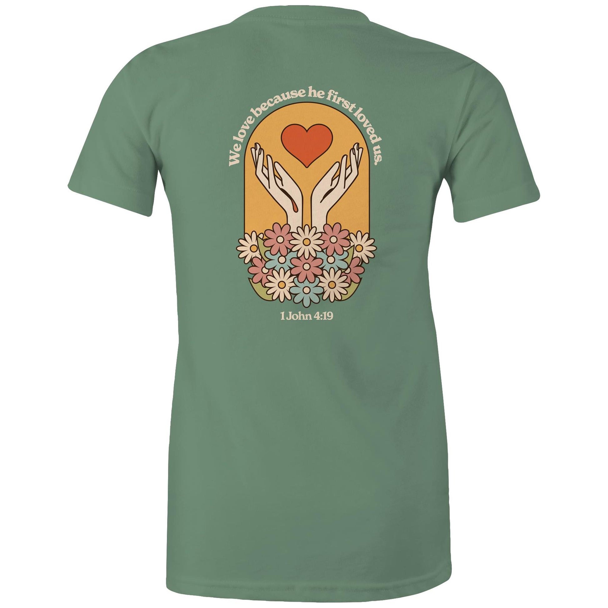 Christian t-shirt with bold faith-based design on the back featuring a red heart, outstretched hands, and colorful flowers. Includes the Bible verse “We love because he first loved us – 1 John 4:19.” Designed by Lighthouse Christian Clothing to inspire love and faith.